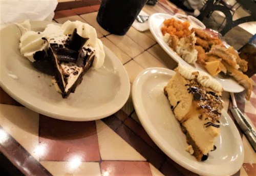 Two dessert plates on a table: one with chocolate pie topped with whipped cream, the other with cheesecake drizzled in chocolate.