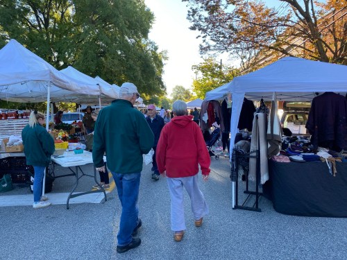 A bustling outdoor market with tents, shoppers, and various goods displayed on tables under clear skies.