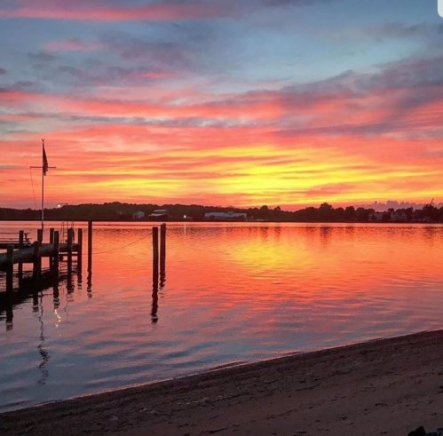 A vibrant sunset over a calm lake, with colorful clouds reflecting on the water and a silhouette of a dock.
