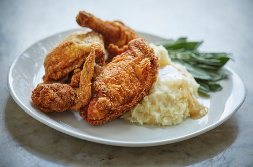 A plate of crispy fried chicken with creamy mashed potatoes and green leaves on the side.