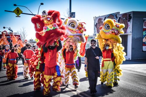 A vibrant parade featuring performers in colorful lion costumes, walking down the street with festive decorations.