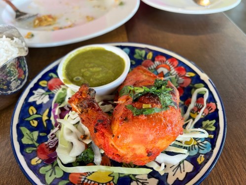 A vibrant plate featuring a piece of tandoori chicken on a bed of cabbage, accompanied by green chutney.