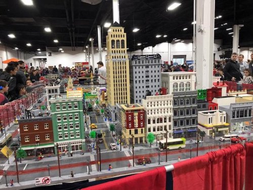 A detailed LEGO cityscape with buildings, streets, and mini figures, displayed at a crowded event.