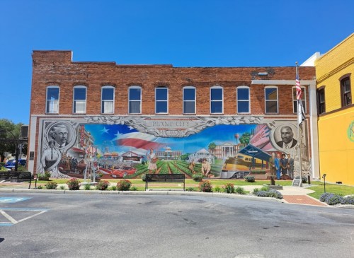 Colorful mural on a brick building depicting historical scenes and figures from Miami City, under a clear blue sky.