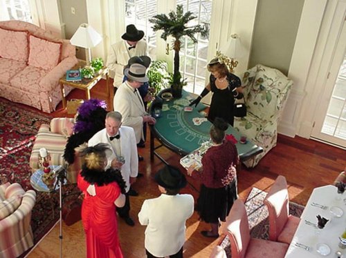 A group of elegantly dressed people playing cards in a stylish, well-decorated room with a palm tree centerpiece.