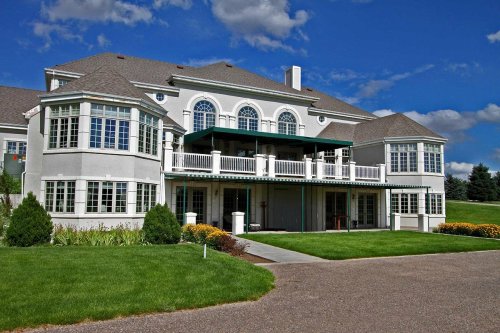 A large, elegant house with multiple windows, a balcony, and a well-maintained lawn under a blue sky.