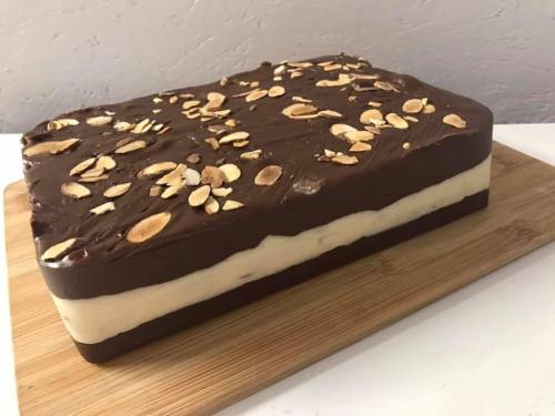A rectangular layered cake with chocolate frosting and sliced almonds on top, resting on a wooden board.