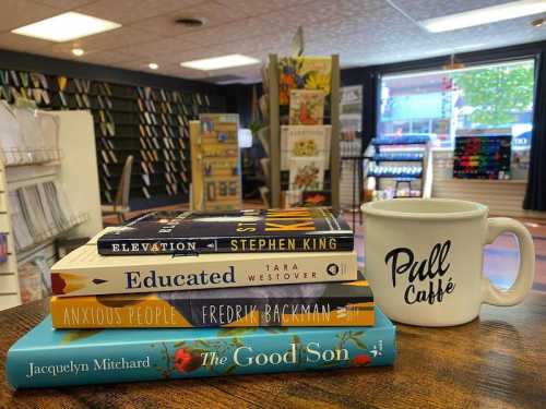 A stack of books with a coffee mug on a table in a cozy bookstore setting.