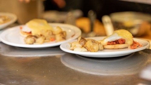 Two plates of food featuring eggs Benedict with potatoes on a countertop.