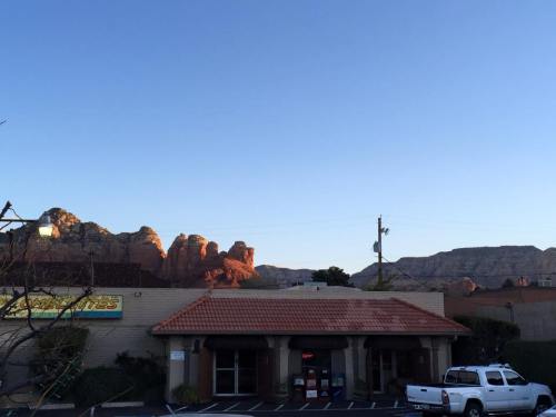 A building with a red-tiled roof in the foreground, surrounded by rocky mountains and a clear blue sky in the background.