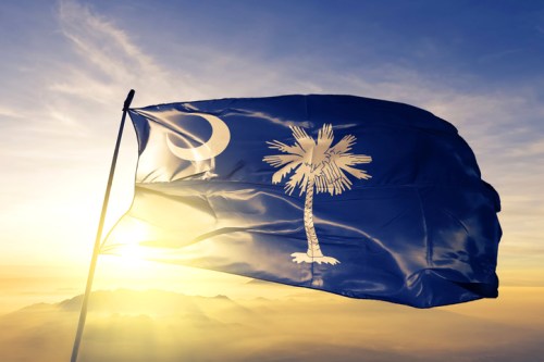 South Carolina state flag waving against a sunset backdrop with mountains in the distance.