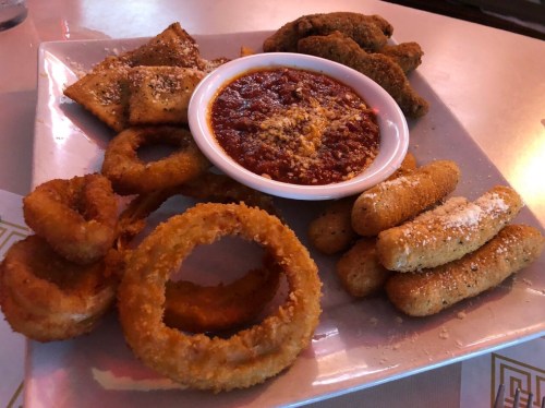 A platter of assorted appetizers including onion rings, mozzarella sticks, and dipping sauce.