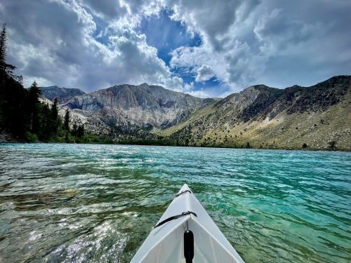 A kayak on clear turquoise water, surrounded by mountains and a dramatic sky with clouds.