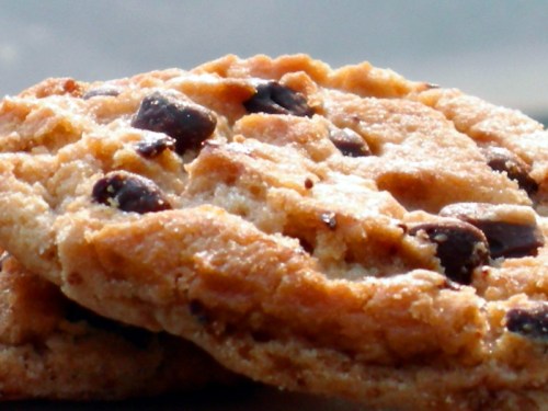Close-up of two golden-brown cookies with chocolate chips, showcasing a crispy texture and a soft interior.