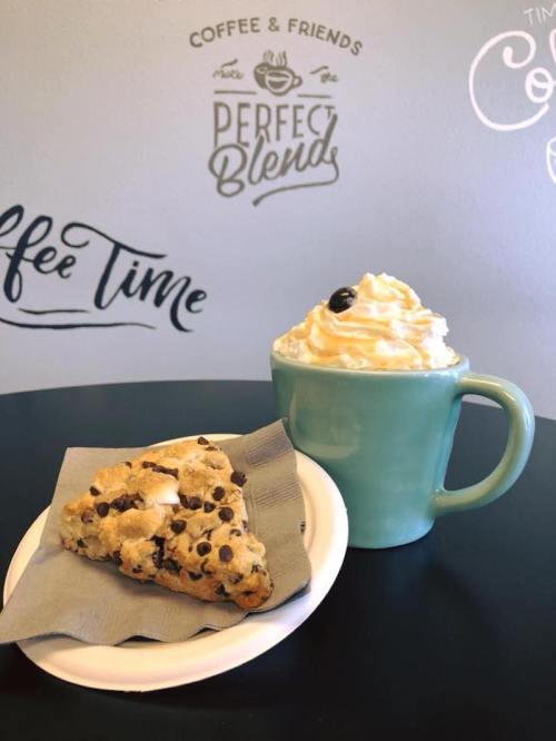 A plate with a chocolate chip scone next to a teal mug filled with whipped cream and a coffee drink.
