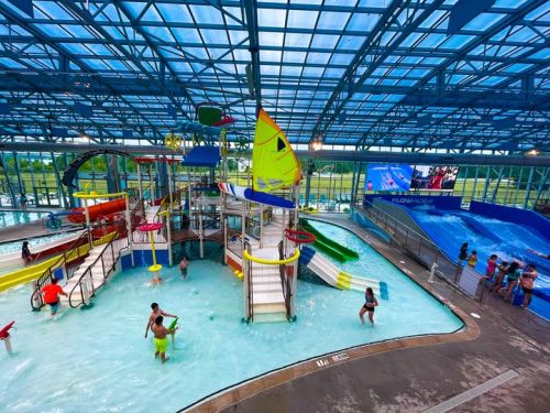 Indoor water park featuring slides, a play structure, and a wave pool, with people enjoying the attractions.