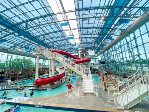 Indoor water park featuring a large red waterslide, pools, and people enjoying the water. Bright, spacious environment.