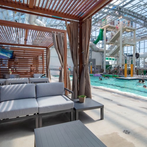 Indoor water park scene with seating areas, water slides, and people enjoying the pool. Bright and spacious atmosphere.