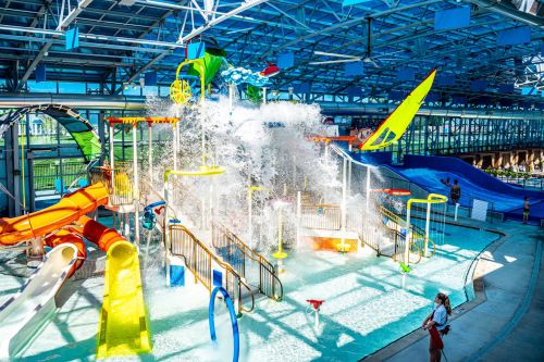 A vibrant indoor water park featuring colorful slides, splash pads, and water features, with people enjoying the attractions.