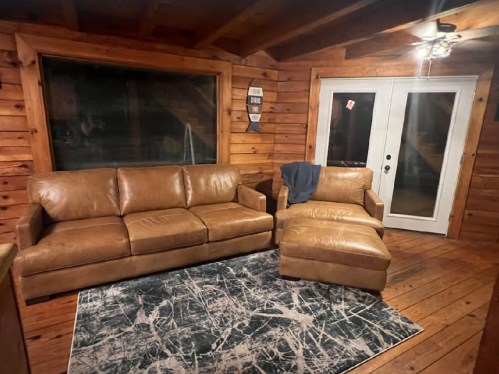 Cozy wooden room featuring a brown leather sofa, a chaise lounge, and a patterned rug near glass doors.