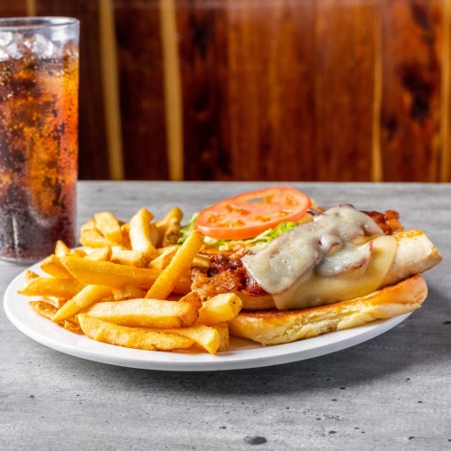 A plate with a sandwich topped with cheese, lettuce, and tomato, served with fries and a glass of soda in the background.