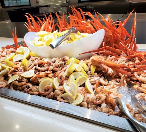 A seafood display featuring shrimp, crab legs, and lemon wedges on ice, arranged in a large bowl.