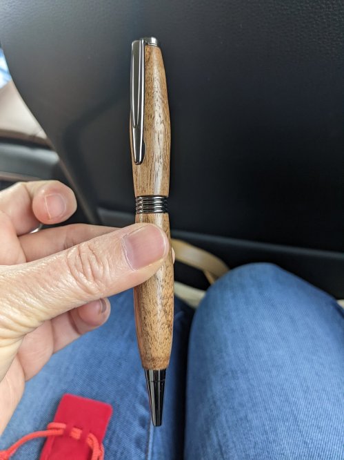 A person holding a wooden pen with a silver clip, sitting in a car with denim visible in the background.