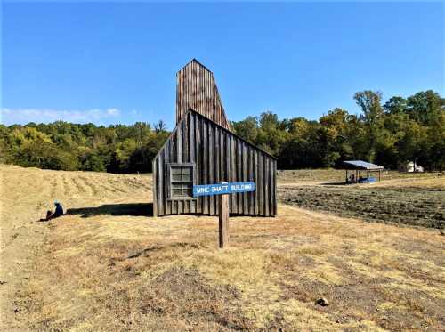 A wooden building with a slanted roof, labeled "Mine Shaft Building," set in a dry, grassy landscape.