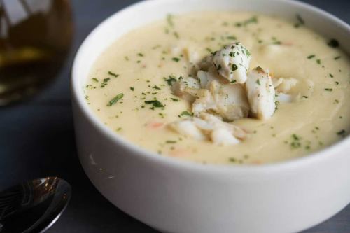 A creamy soup topped with chunks of white fish and sprinkled with herbs, served in a white bowl.