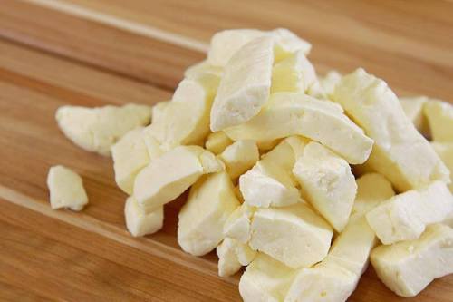 A pile of small, irregularly shaped pieces of yellow cheese on a wooden surface.