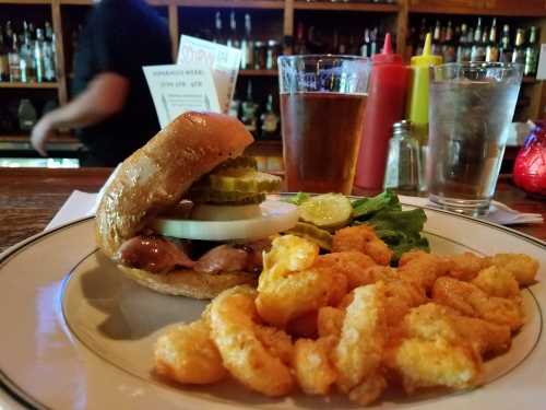 A plate with a burger topped with pickles and onions, served with a side of cheese curds and a glass of beer.