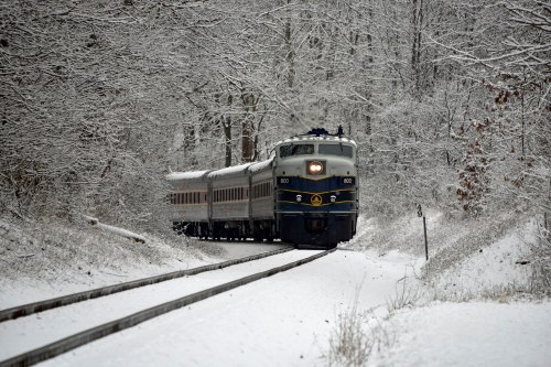 A vintage train travels through a snowy landscape, surrounded by trees blanketed in white.