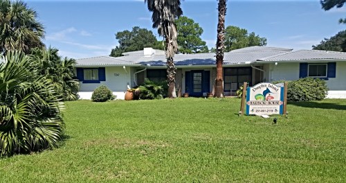 A single-story house with a landscaped yard, palm trees, and a sign reading "Dolphin's Retreat" in front.