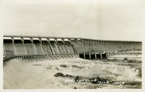 Black and white photo of the American Falls Dam in Idaho, showcasing rushing water and the dam's structure.