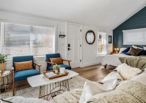 Cozy living space with blue chairs, a white coffee table, and a bed in a bright, modern room with natural light.