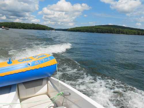 A view from a boat on a lake, with waves trailing behind and green hills in the background under a partly cloudy sky.