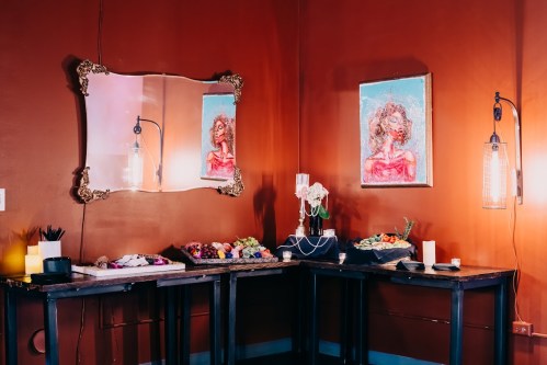 A cozy room with a mirror, artwork, and tables displaying colorful floral arrangements and decorative items.