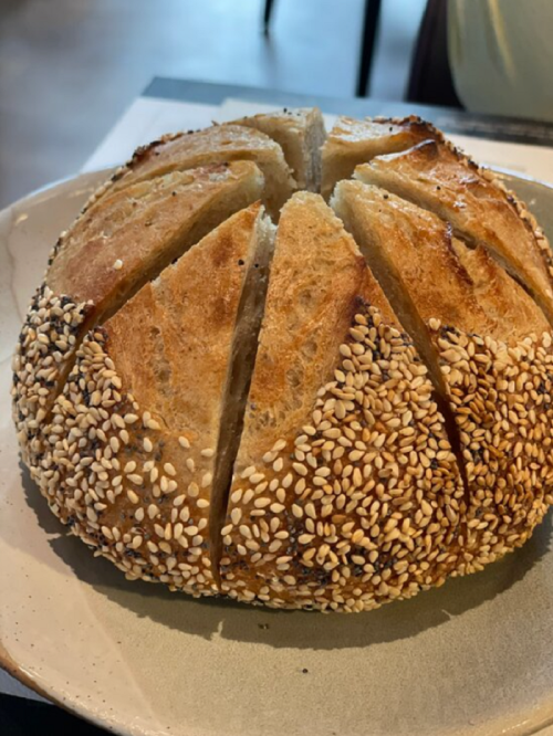 A round loaf of bread with a sesame seed crust, scored on top, resting on a plate.