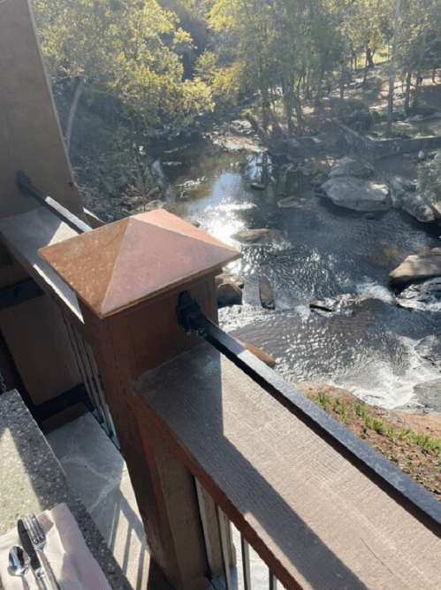 View from a balcony overlooking a serene river with rocks and trees in the background, reflecting sunlight.