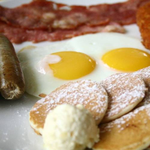 A plate with two sunny-side-up eggs, sausage, bacon, and pancakes with butter and syrup.