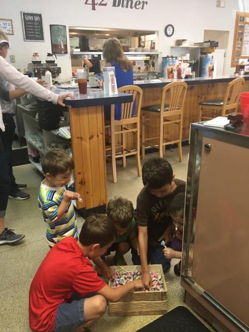 A group of children gathers around a basket, exploring its contents in a diner with a casual atmosphere.