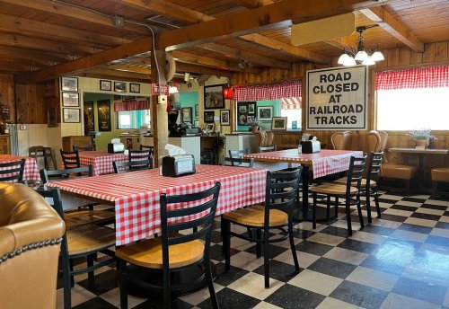 Cozy diner interior with checkered tablecloths, wooden beams, and vintage decor, featuring a "Road Closed" sign.