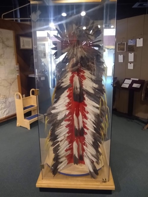 A feathered headdress displayed in a glass case, showcasing intricate designs and vibrant colors.