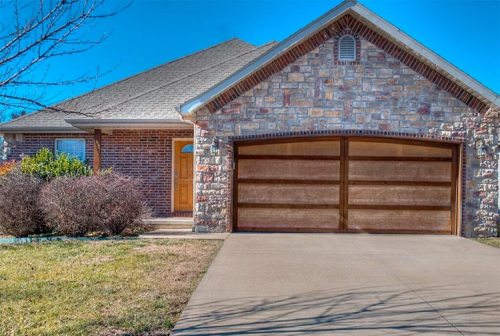 A brick and stone house with a wooden garage door and a clear blue sky in the background.