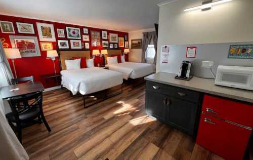 A cozy hotel room with two beds, a kitchenette, and colorful wall art. Warm lighting enhances the inviting atmosphere.