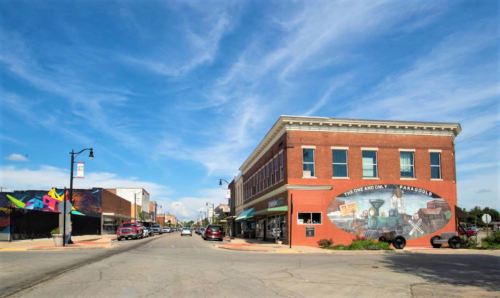 A vibrant street scene featuring a brick building with a mural, under a blue sky with scattered clouds.
