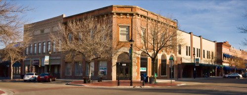 Historic brick buildings line a street, with bare trees and blue awnings under a clear sky.