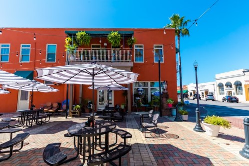 A vibrant outdoor seating area with umbrellas, surrounded by colorful buildings and palm trees under a clear blue sky.