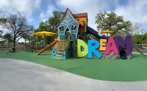 Colorful playground with a slide and a large "DREAM" sign, surrounded by trees and blue skies.