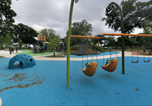 Colorful playground with swings, a climbing structure, and a blue rubber surface under a cloudy sky.
